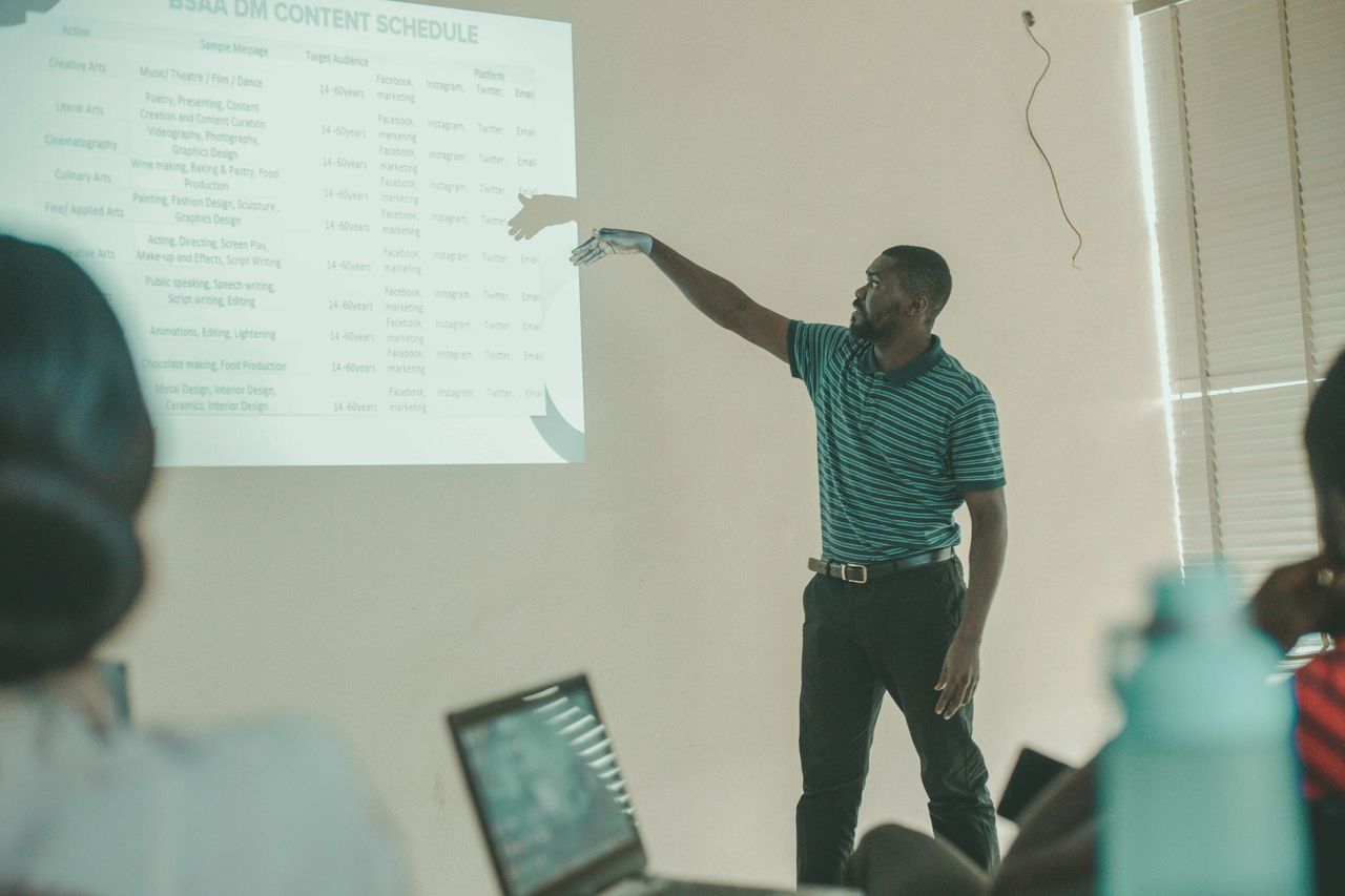Man presenting business schedule to a class using a projector, engaging students.