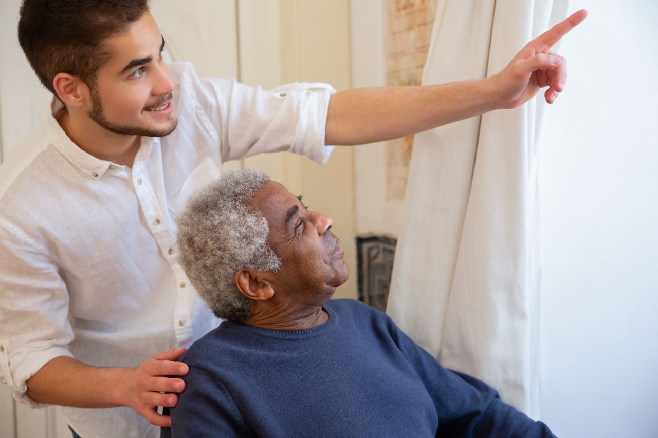 Young man assisting and engaging with senior indoors.